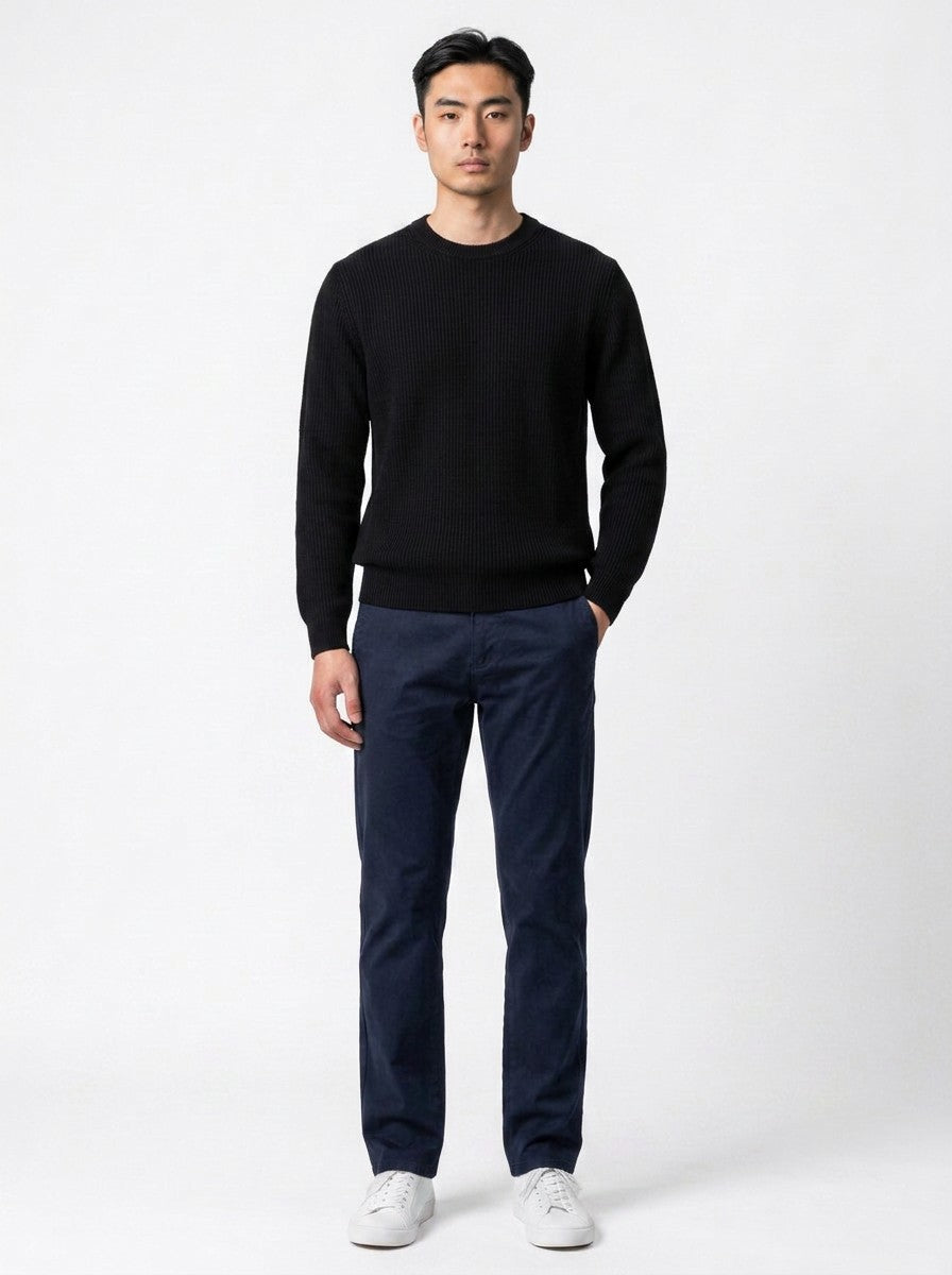 Modelo vestindo calça chino azul marinho Bluviso com suéter preto e tênis brancos em fundo neutro