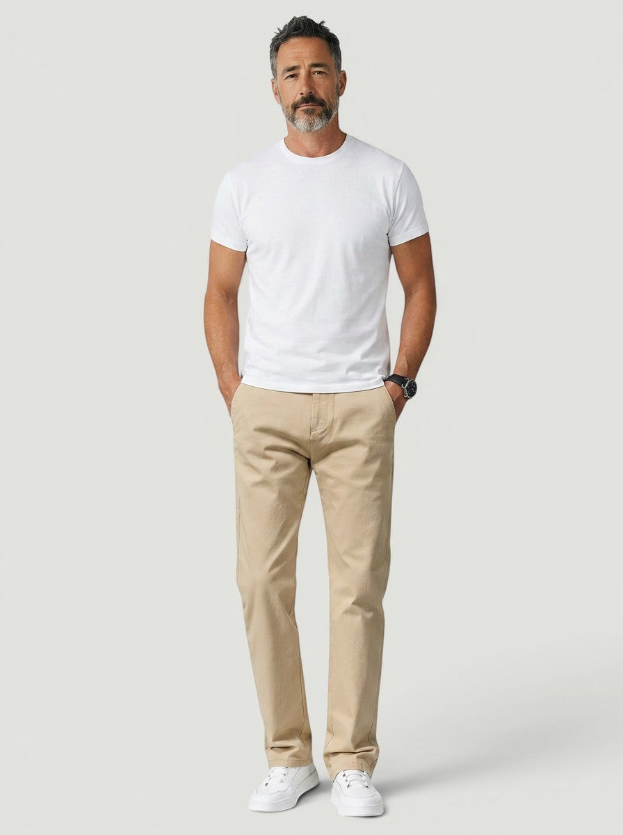 Homem vestindo calça chino bege reta da Bluviso com camiseta branca e tênis em visual casual elegante