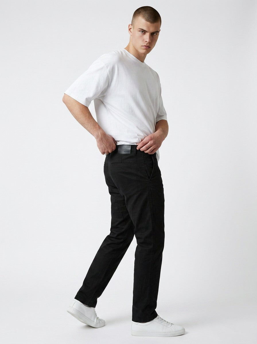 Homem vestindo calça chino em preto Bluviso com camiseta branca e tênis, exibindo corte moderno e ajuste confortável.
