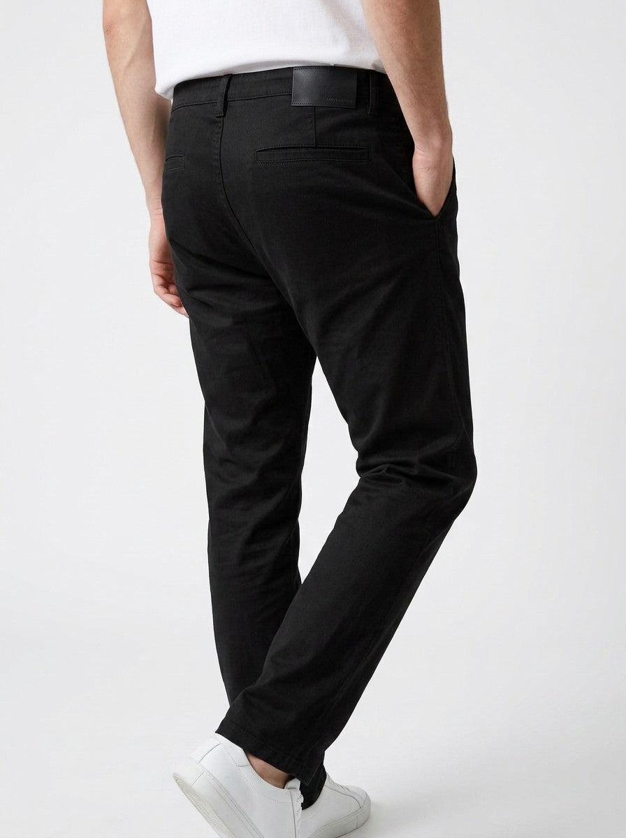 Homem vestindo calça chino em preto Bluviso com camiseta branca e tênis, exibindo corte moderno e ajuste confortável arte traseira.
