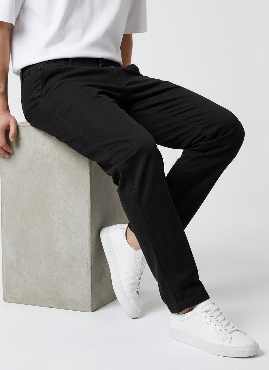 Homem vestindo calça chino em preto Bluviso com camiseta branca e tênis, exibindo corte moderno e ajuste confortável.