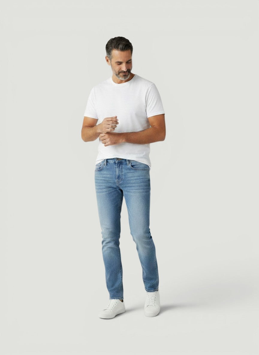 Homem vestindo calça jeans Bluviso de corte ajustado em tom azul claro com camiseta branca e tênis casual