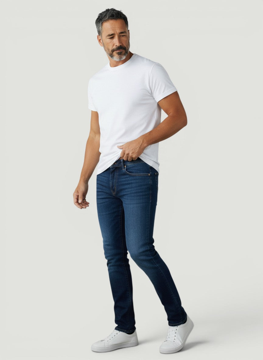 Homem vestindo calça jeans Bluviso de corte ajustado azul escuro com camiseta branca e tênis casual