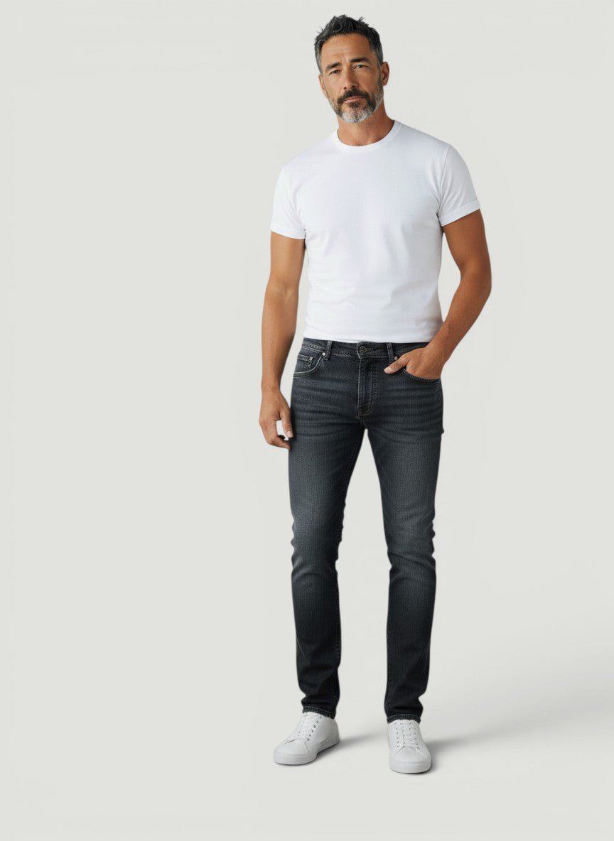 Homem vestindo calça jeans Bluviso preta de corte ajustado com camiseta branca e tênis casual em fundo neutro