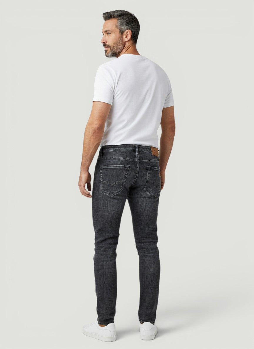 Homem vestindo calça jeans Bluviso cinza de corte ajustado, vista traseira, combinada com camiseta branca e tênis.