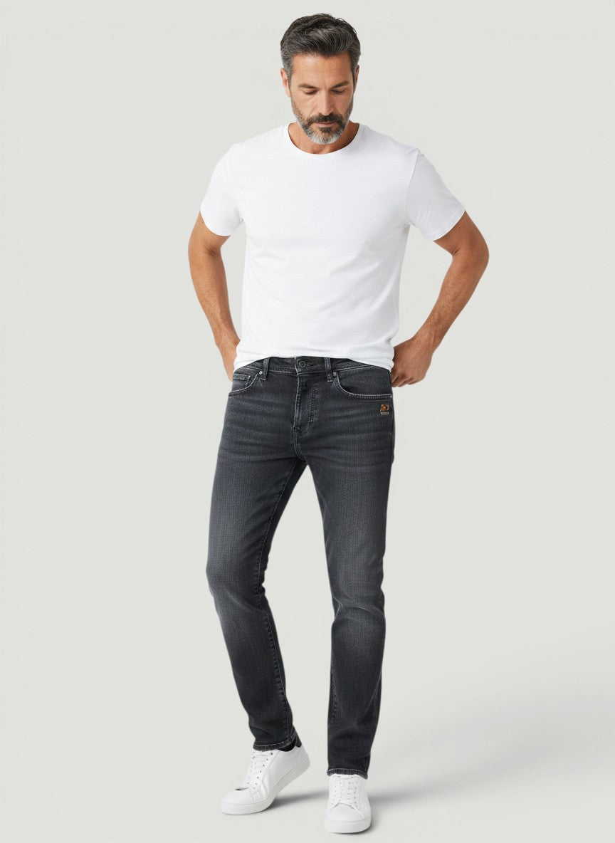 Homem vestindo calça jeans Bluviso preta de corte ajustado com camiseta branca e tênis em fundo neutro
