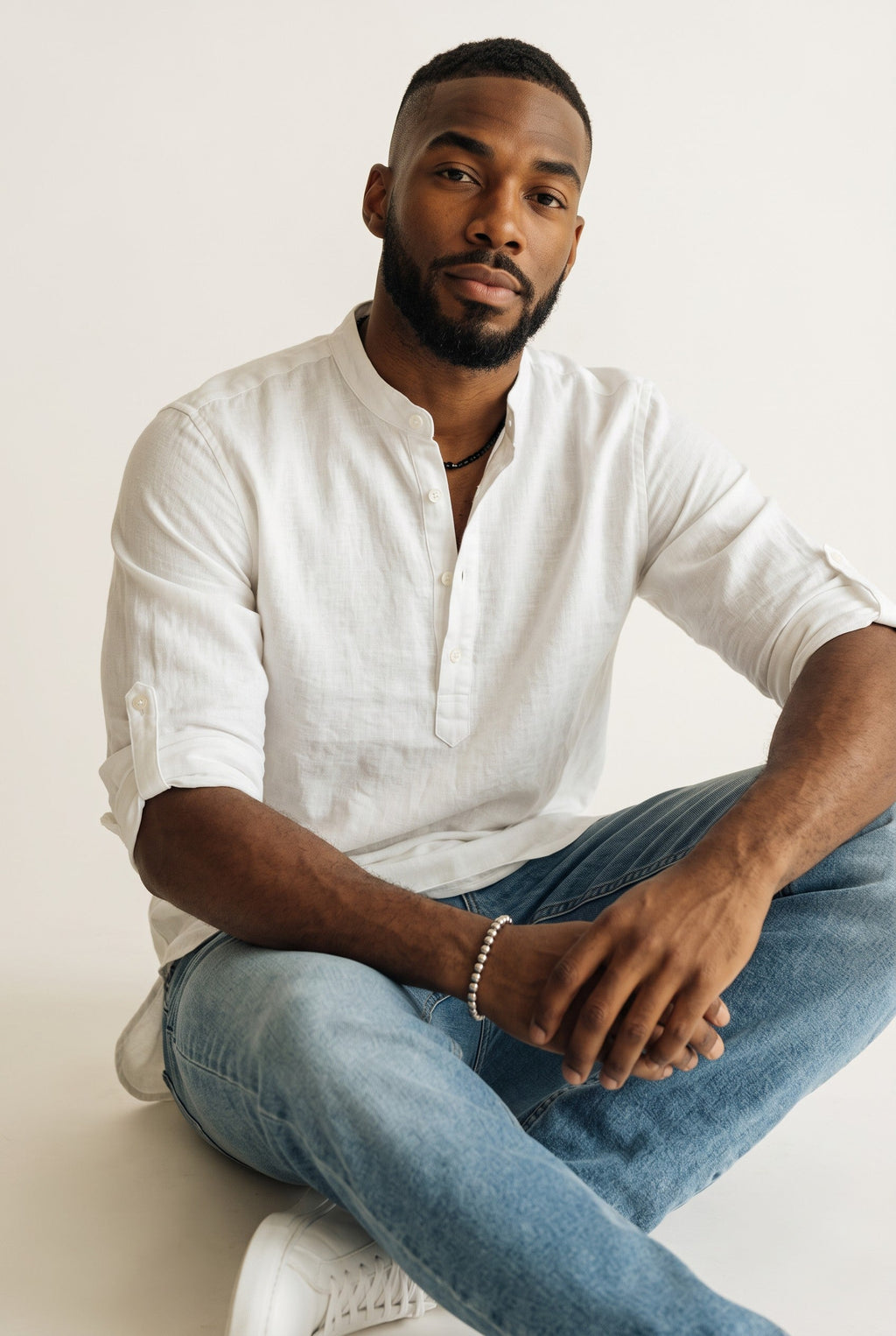 Homem negro vestindo camisa polo Bluviso de manga longa branca em linho e algodão com gola padre e calça jeans clara