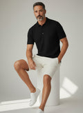 Homem vestindo camisa polo preta texturizada Bluviso com bermuda clara e tênis branco em estúdio