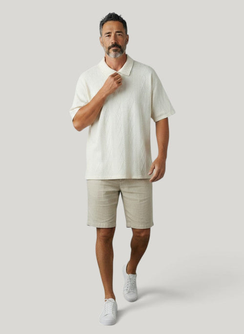 Homem vestindo camisa polo Bluviso off-white com textura em relevo, bermuda bege e tênis branco em fundo neutro.