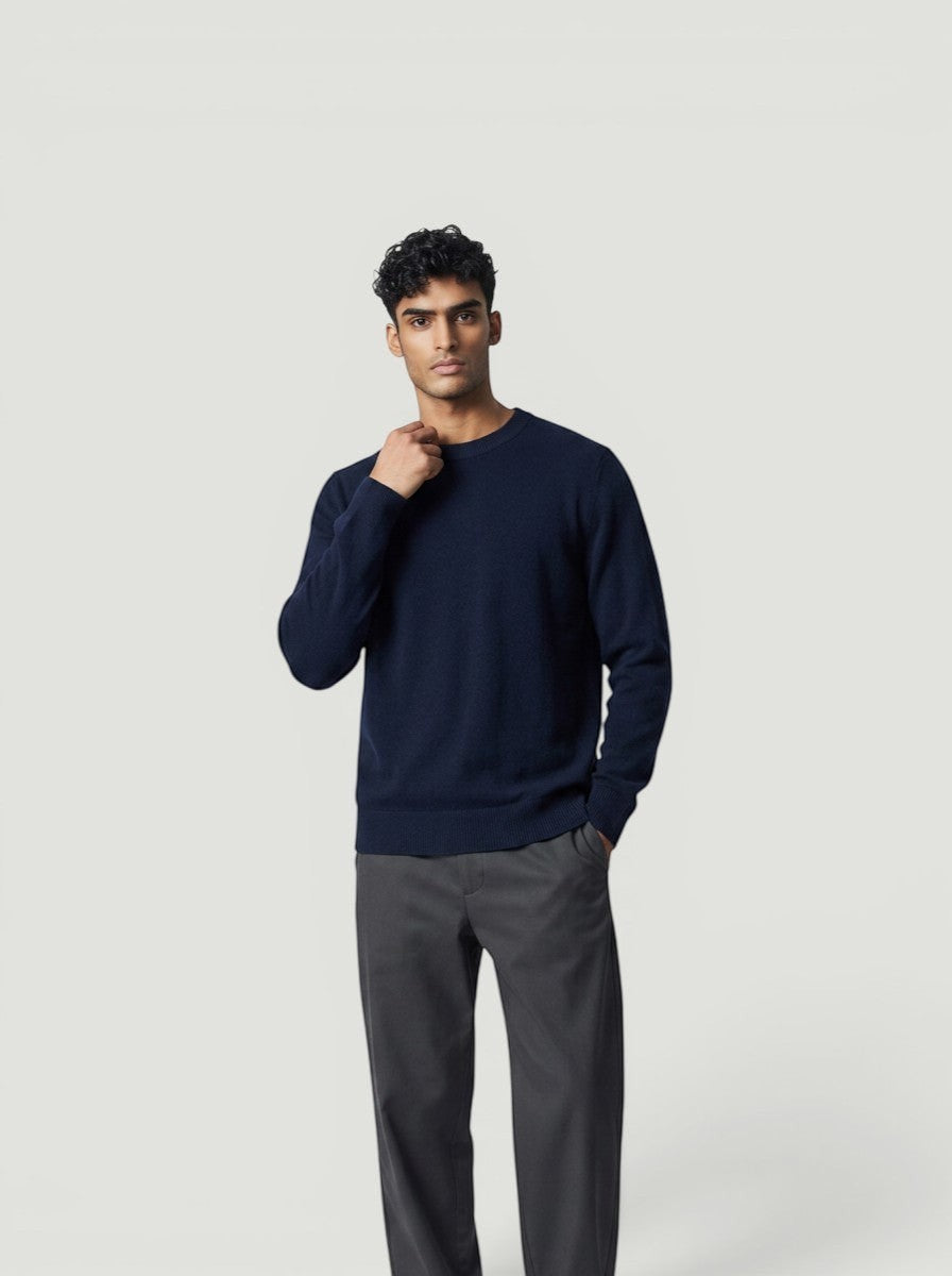 Modelo vestindo suéter de tricô Bluviso azul marinho com gola careca, calça cinza e tênis branco em fundo neutro.